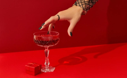 женщина тянет руку к бокалу с алкоголем