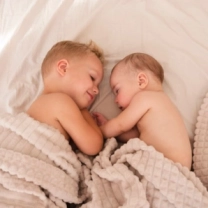 два близнеца лежат на кровати под одеялом